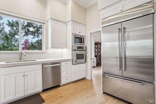 kitchen with sink, built in appliances, white cabinets, and light hardwood / wood-style flooring