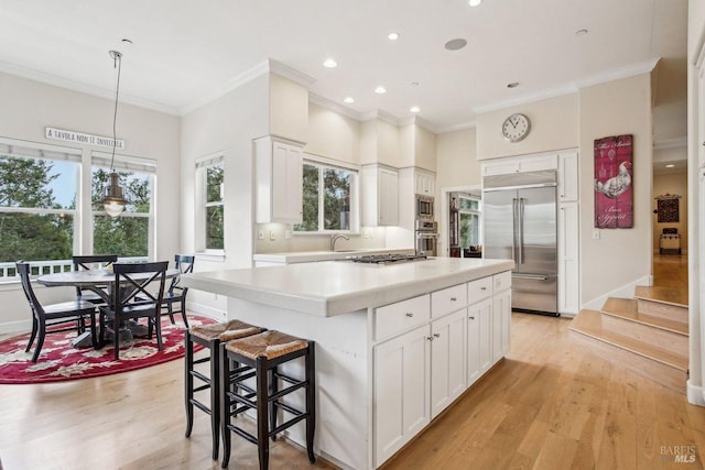 kitchen with pendant lighting, sink, white cabinetry, built in appliances, and a kitchen island