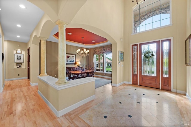 foyer entrance with ornate columns, a high ceiling, light wood-type flooring, and a tray ceiling