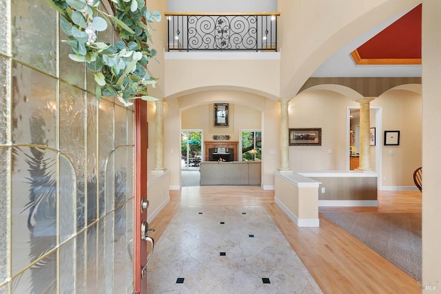 entrance foyer featuring a notable chandelier, a towering ceiling, light hardwood / wood-style floors, and ornate columns