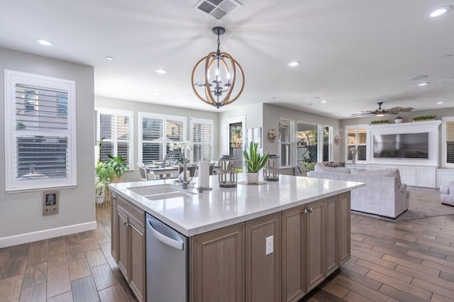 kitchen with an island with sink, dishwasher, sink, hanging light fixtures, and dark wood-type flooring