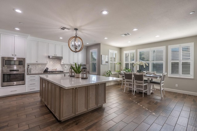 kitchen featuring pendant lighting, stainless steel appliances, a center island, white cabinets, and decorative backsplash