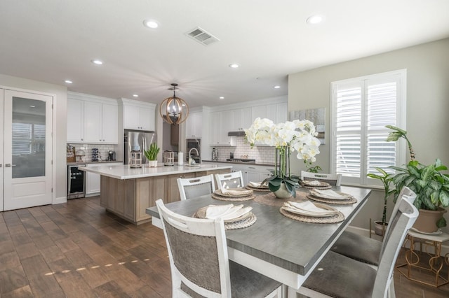 dining space featuring dark hardwood / wood-style floors, sink, beverage cooler, and an inviting chandelier