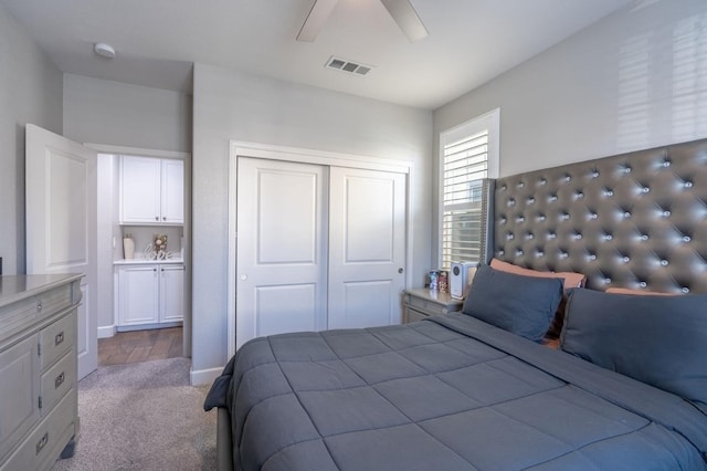 bedroom with ceiling fan, ensuite bath, light carpet, and a closet