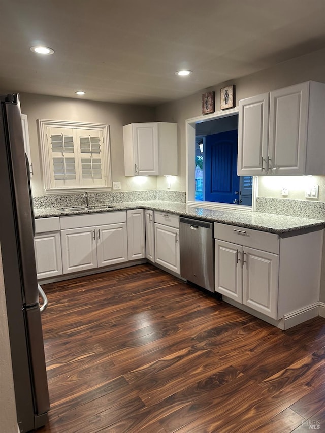 kitchen with sink, appliances with stainless steel finishes, dark hardwood / wood-style floors, light stone countertops, and white cabinets