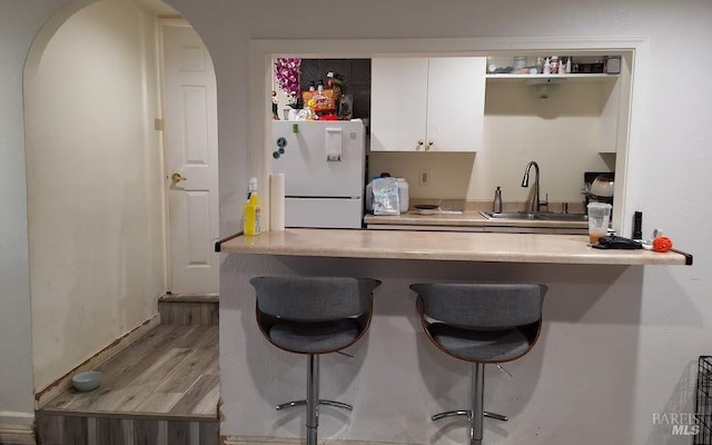 kitchen with sink, white cabinets, a kitchen bar, white fridge, and light wood-type flooring