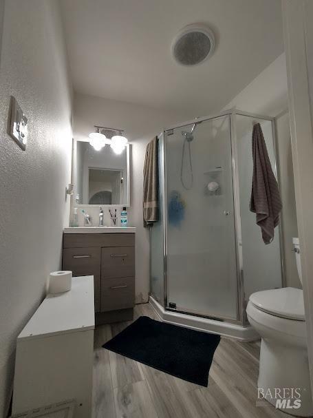 bathroom featuring wood-type flooring, toilet, a shower with door, and vanity