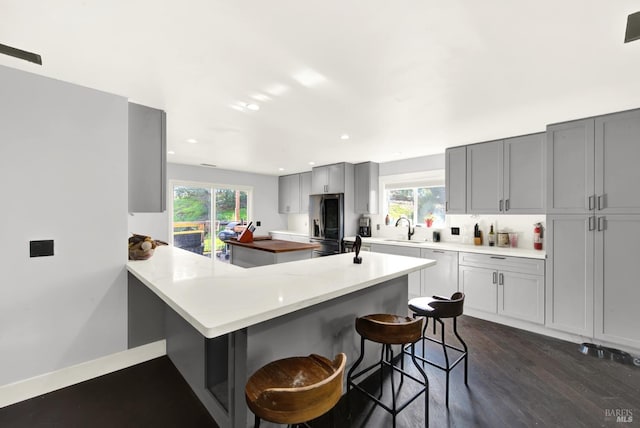 kitchen with gray cabinets, a kitchen breakfast bar, stainless steel refrigerator with ice dispenser, a wealth of natural light, and kitchen peninsula