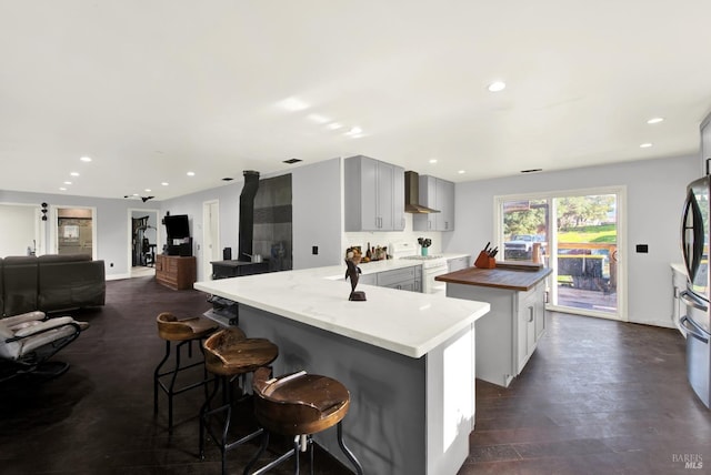 kitchen featuring wall chimney exhaust hood, white range with gas stovetop, gray cabinetry, dark hardwood / wood-style floors, and a kitchen island