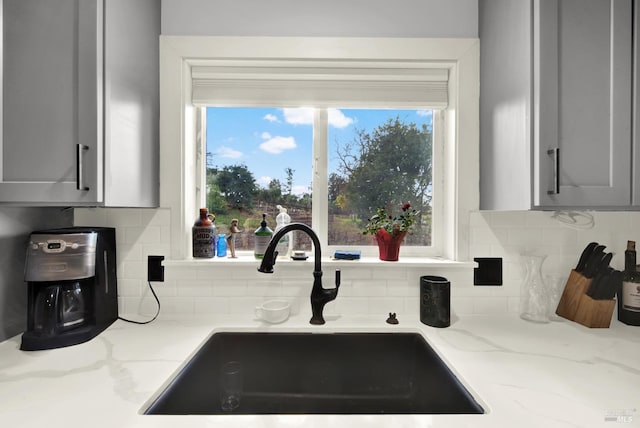 kitchen featuring sink, gray cabinetry, backsplash, and light stone counters