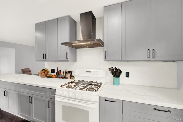 kitchen featuring white gas range, gray cabinetry, light stone counters, and wall chimney exhaust hood