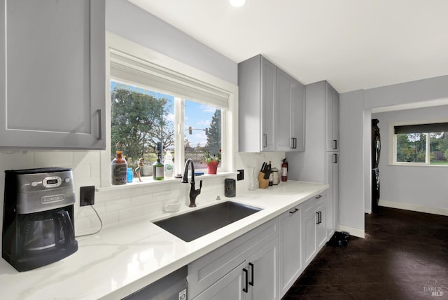 kitchen with gray cabinets, dark hardwood / wood-style floors, tasteful backsplash, sink, and light stone countertops