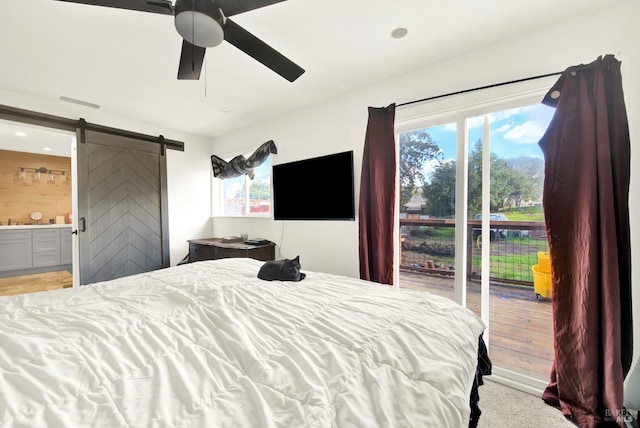 bedroom with multiple windows, ensuite bathroom, a barn door, and access to outside