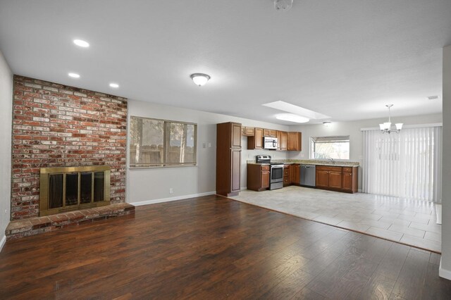 kitchen with decorative light fixtures, wood-type flooring, stainless steel appliances, a brick fireplace, and an inviting chandelier