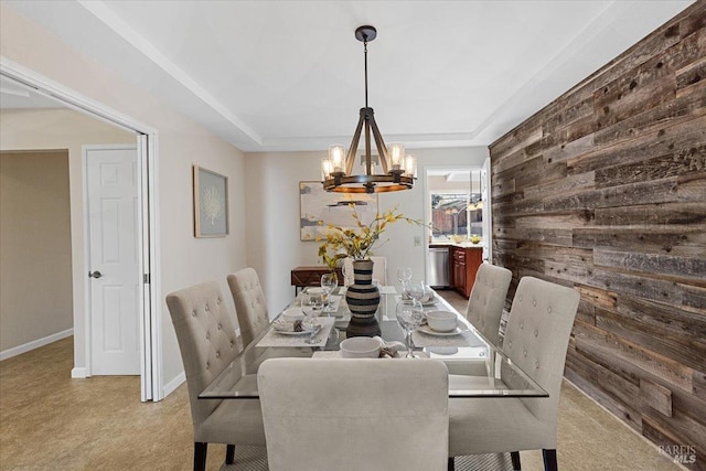 dining room featuring a chandelier, a raised ceiling, and wood walls