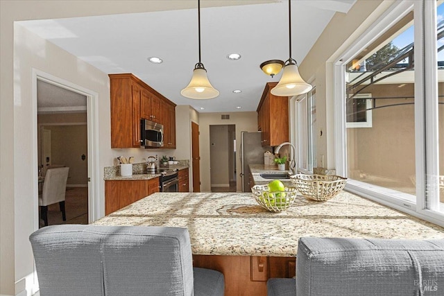 kitchen with a kitchen bar, sink, light stone counters, decorative light fixtures, and stainless steel appliances