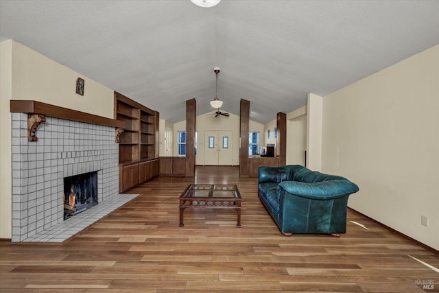 living room featuring built in shelves, vaulted ceiling, a textured ceiling, light wood-type flooring, and a fireplace