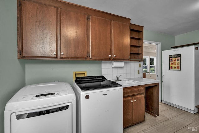 clothes washing area with cabinets, sink, washing machine and dryer, and light wood-type flooring