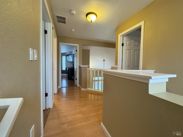 hallway featuring light hardwood / wood-style floors and a textured ceiling