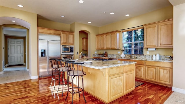 kitchen featuring built in appliances, light brown cabinets, a center island, and light stone countertops