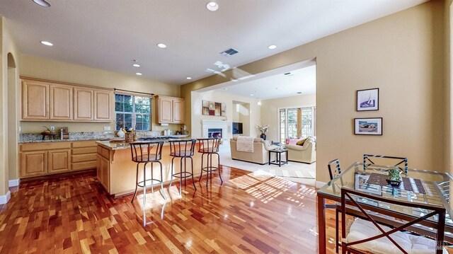 kitchen with a kitchen island, light brown cabinetry, wood-type flooring, a kitchen breakfast bar, and light stone countertops