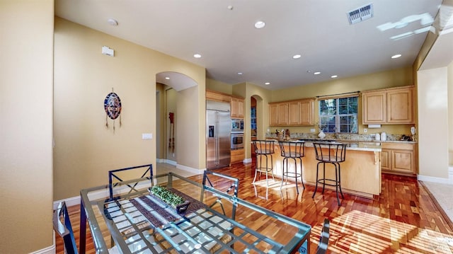 kitchen featuring light wood finished floors, visible vents, arched walkways, built in appliances, and light brown cabinets