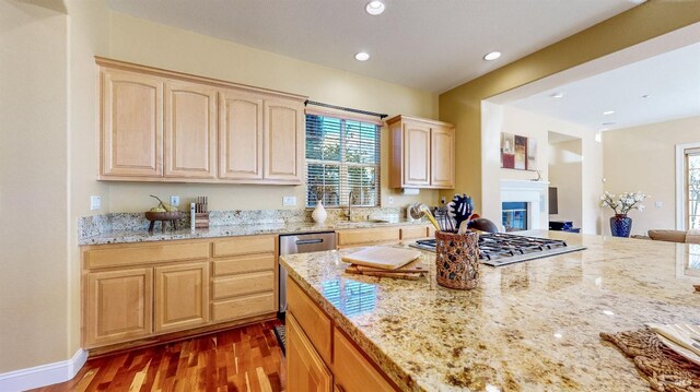 kitchen with appliances with stainless steel finishes, sink, dark hardwood / wood-style flooring, light stone countertops, and light brown cabinets