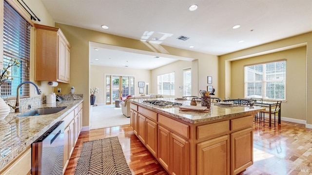 kitchen featuring light stone counters, stainless steel appliances, visible vents, open floor plan, and a sink