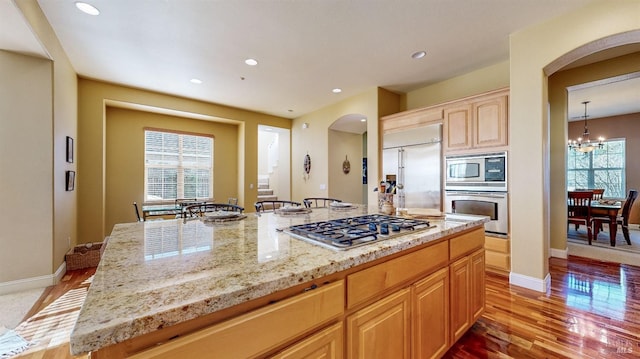 kitchen with light wood-type flooring, arched walkways, light brown cabinetry, and built in appliances