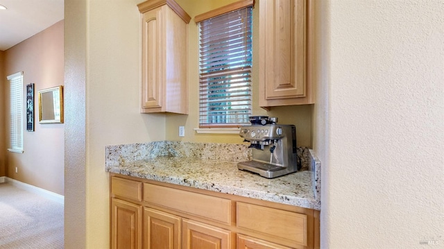 kitchen featuring carpet floors, light stone counters, light brown cabinets, and baseboards