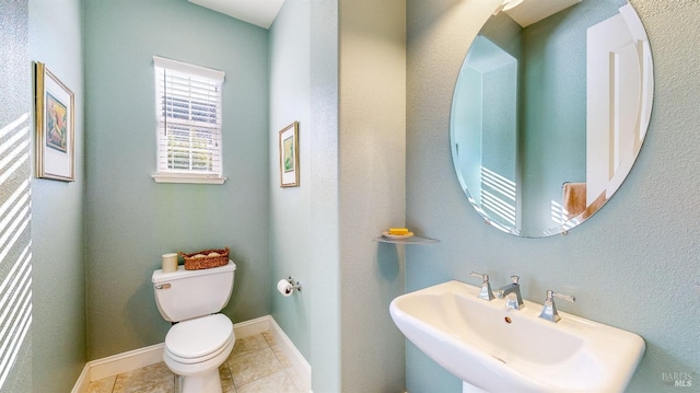 half bath with tile patterned flooring, baseboards, a sink, and toilet