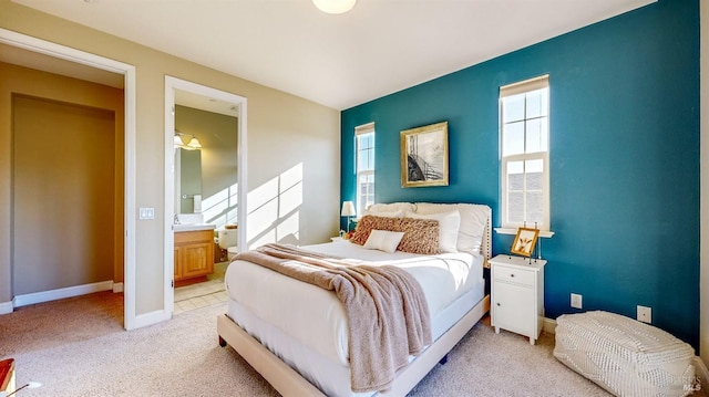 bedroom featuring light colored carpet, ensuite bath, baseboards, and multiple windows