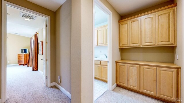 hall featuring light carpet, visible vents, and baseboards