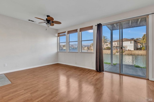 spare room with a water view, ceiling fan, a healthy amount of sunlight, and hardwood / wood-style floors