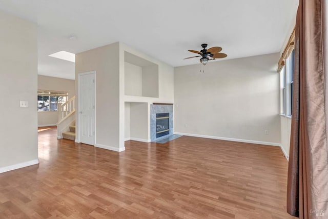 unfurnished living room featuring ceiling fan, a tiled fireplace, and light wood-type flooring