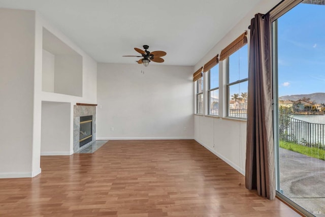 unfurnished living room featuring a water view, ceiling fan, a tile fireplace, and light wood-type flooring