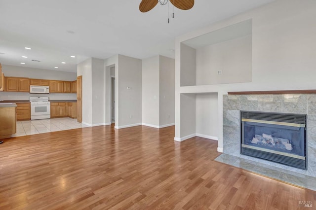 unfurnished living room with ceiling fan, a fireplace, and light hardwood / wood-style flooring