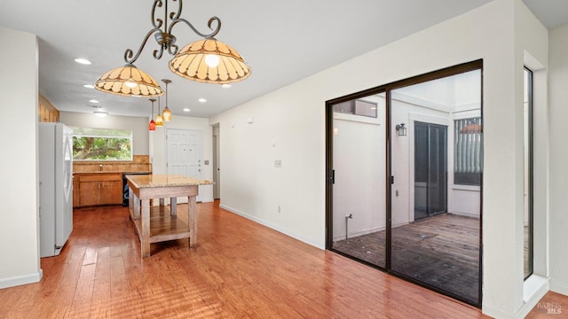 kitchen with light wood finished floors, a kitchen island, recessed lighting, white fridge with ice dispenser, and hanging light fixtures