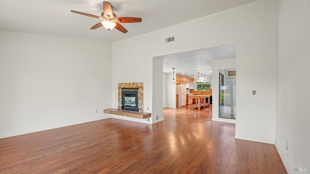 unfurnished living room with wood finished floors, baseboards, visible vents, a ceiling fan, and a tiled fireplace