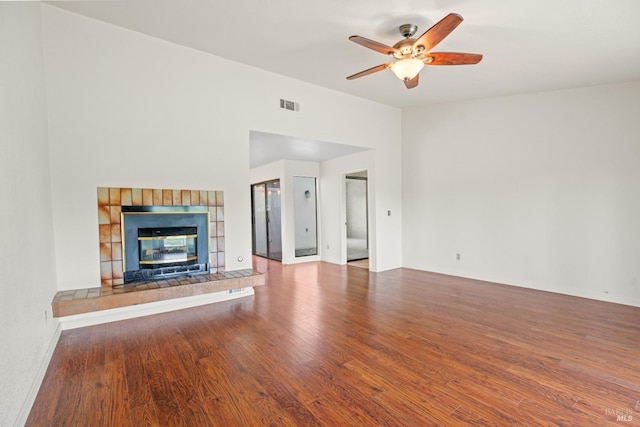 unfurnished living room featuring a tiled fireplace, visible vents, a ceiling fan, and wood finished floors