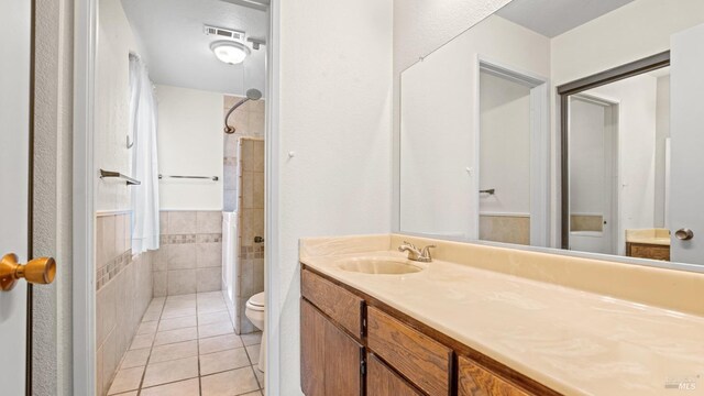 bathroom featuring tile walls, toilet, tiled shower, tile patterned floors, and vanity