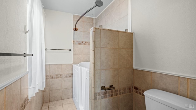 bathroom featuring toilet, tile walls, tile patterned flooring, and a tile shower