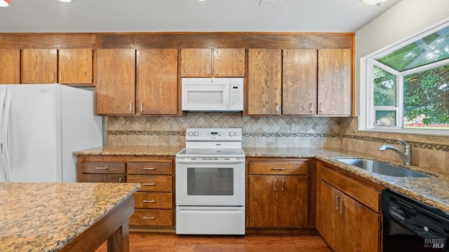 kitchen featuring white appliances, brown cabinetry, backsplash, and a sink