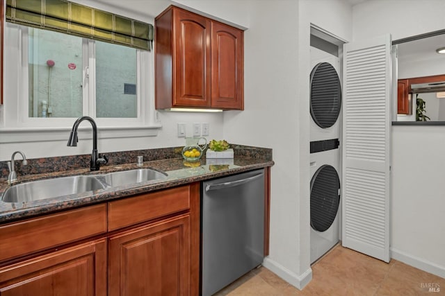 kitchen featuring dishwasher, dark stone counters, stacked washer / drying machine, light tile patterned floors, and sink