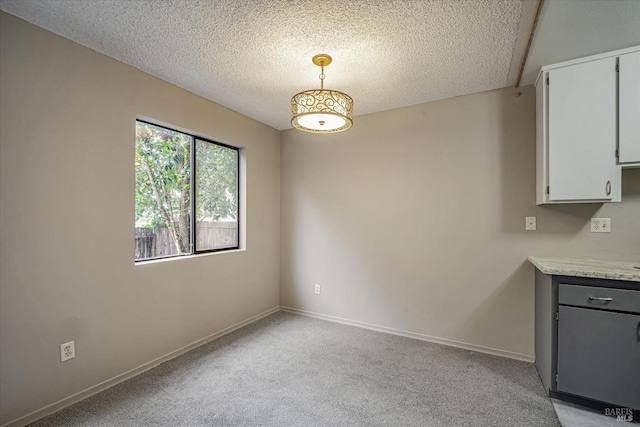 unfurnished dining area with baseboards, light carpet, and a textured ceiling