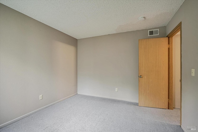 carpeted empty room featuring visible vents, a textured ceiling, and baseboards