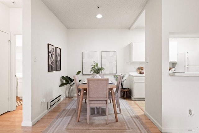 dining space with light wood-type flooring, a textured ceiling, and a baseboard heating unit