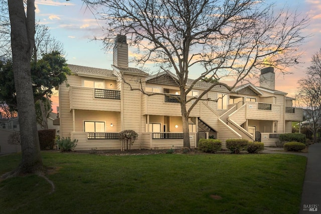 view of front of home with a balcony, a chimney, and a front yard