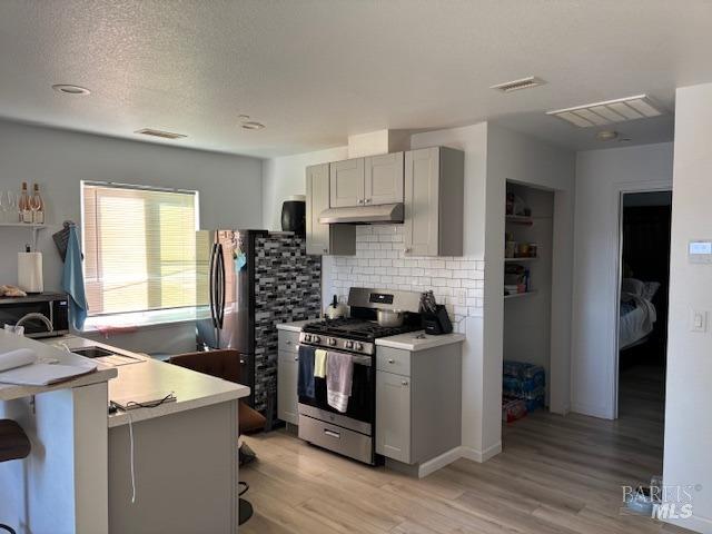 kitchen featuring gray cabinetry, tasteful backsplash, stainless steel gas range oven, a kitchen breakfast bar, and light hardwood / wood-style floors