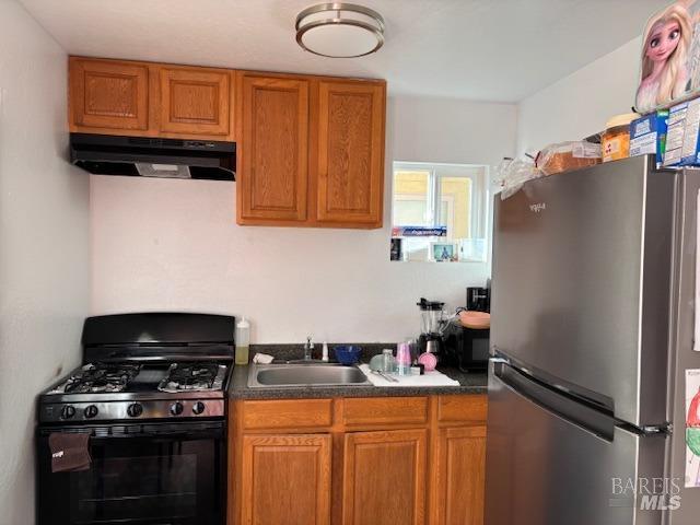 kitchen featuring black gas range oven, sink, and stainless steel fridge